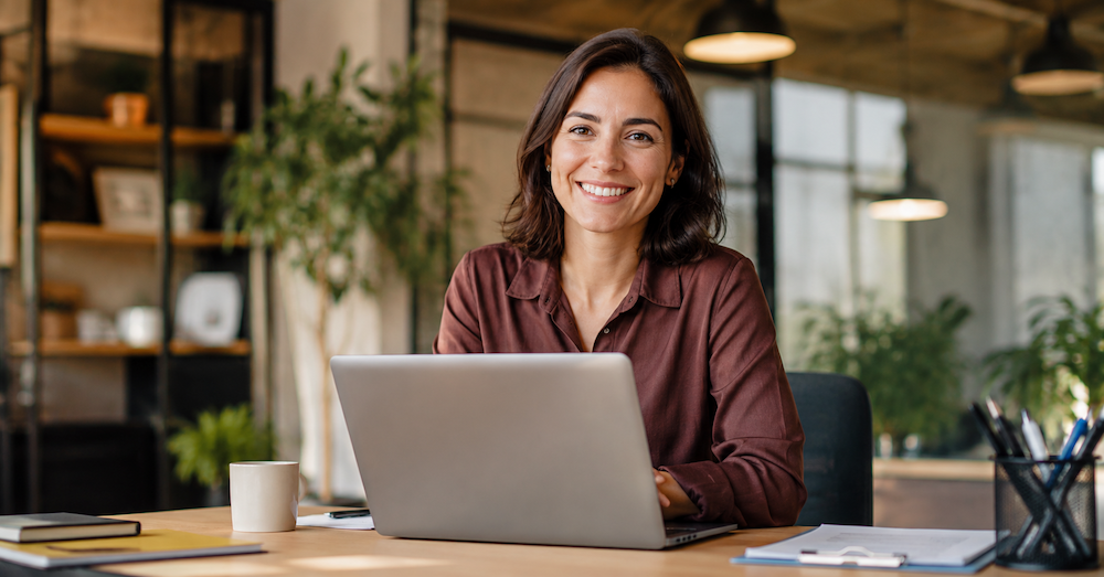 Femme souriante derrière son ordinateur vous regarde
